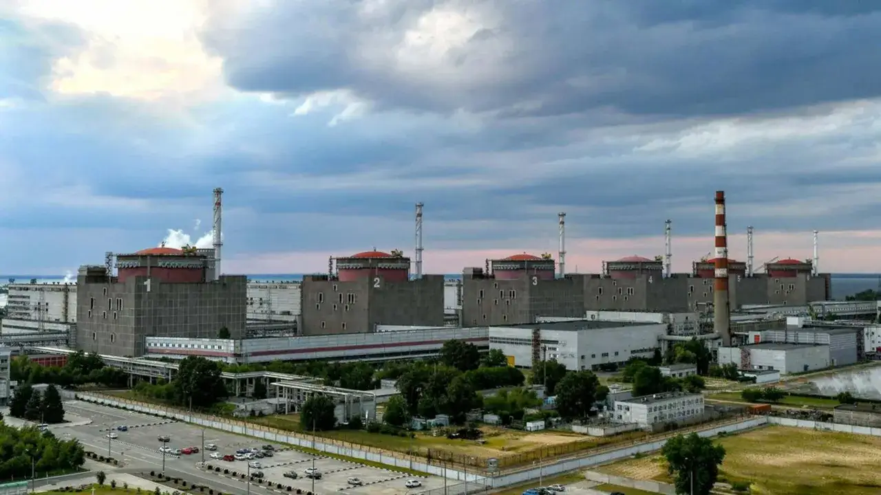 Ogromna elektrownia jądrowa Zaporoże z sześcioma reaktorami pod czerwonymi kopułami, otoczona zielenią i parkingami.