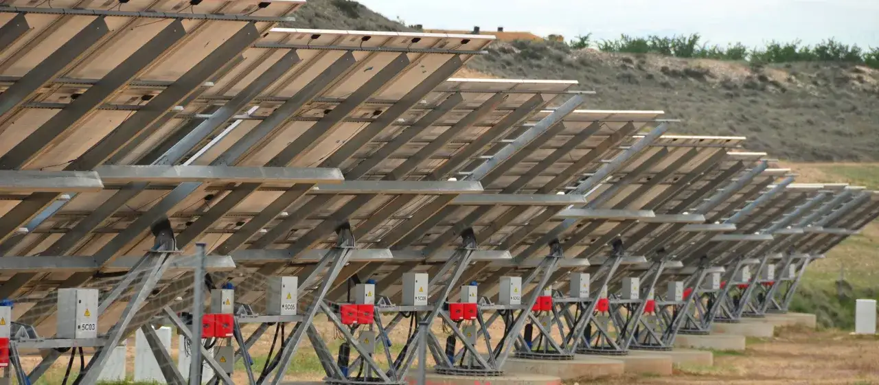 Rzędy paneli słonecznych na krańcówce farmy fotowoltaicznej, widok od spodu. Metalowe konstrukcje i skrzynki elektryczne.