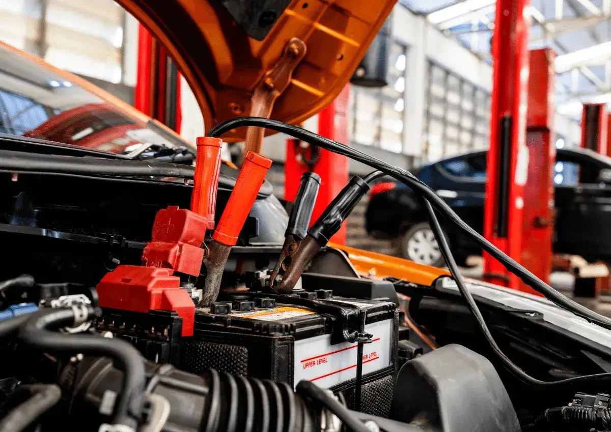 Kable rozruchowe podłączone do akumulatora samochodowego. W warsztacie samochodowym, gdzie mechanik zastanawia się, jakim prądem ładować akumulator.