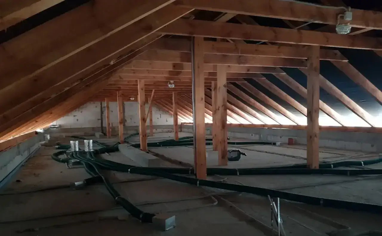 Instalacja rekuperacji w starym domu. Drewniana więźba dachowa, betonowe ściany i zielone przewody wentylacyjne tworzą nowoczesny system w zabytkowej przestrzeni.