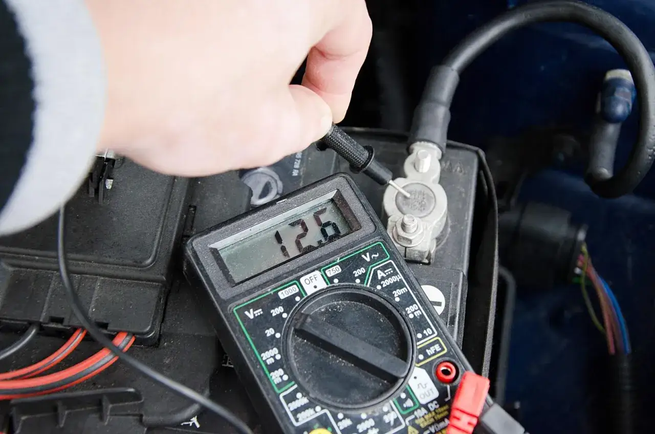 Ręka mierzy napięcie akumulatora multimetrem. Wynik 12.6V wskazuje na dobry stan.