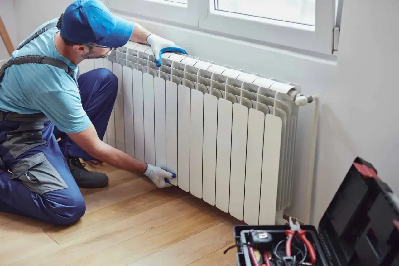 Instalator sprawdza, dlaczego najdalszy grzejnik nie grzeje. Obok stoi skrzynka z narzędziami.