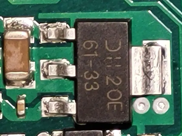 Czarny element z oznaczeniem "DH 20E 61-33" to elektroda tranzystora, otoczona innymi komponentami na zielonej płytce drukowanej.