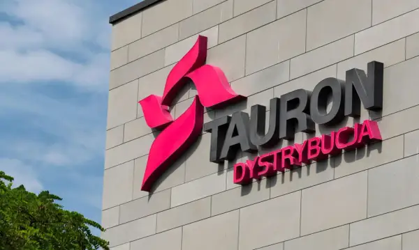 Logo Tauron Dystrybucja na szarej ścianie budynku. Zwiększenie mocy przyłączeniowej Tauron to klucz do rozwoju.