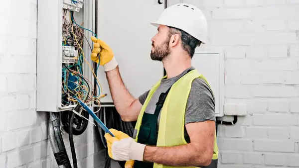 Elektryk w kasku i kamizelce odblaskowej pracuje przy skrzynce z przewodami. Sprawdź nasz **usługi elektryczne cennik**!