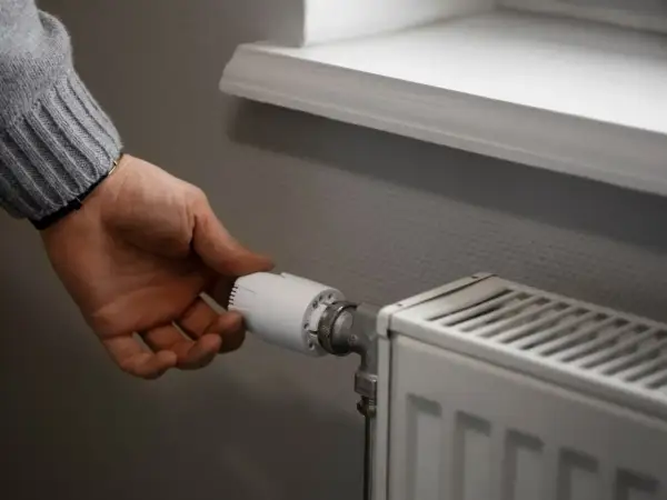 Dłoń reguluje termostat grzejnika, by zapewnić optymalną temperaturę w pomieszczeniu.