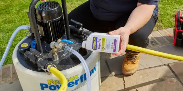 Osoba dodaje środek do czyszczenia instalacji co do urządzenia Fernox Powerflow.