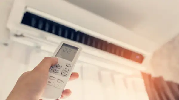 Dłoń trzymająca pilot do klimatyzacji z widoczną temperaturą 22 stopnie.