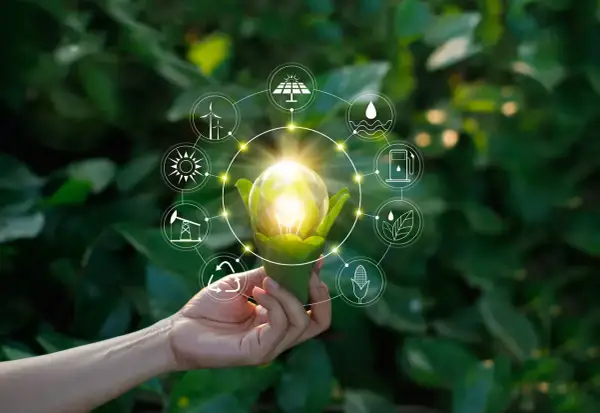 Dłoń trzyma żarówkę z zielonymi liśćmi, otoczoną ikonami symbolizującymi różne źródła energii, w tym OZE.